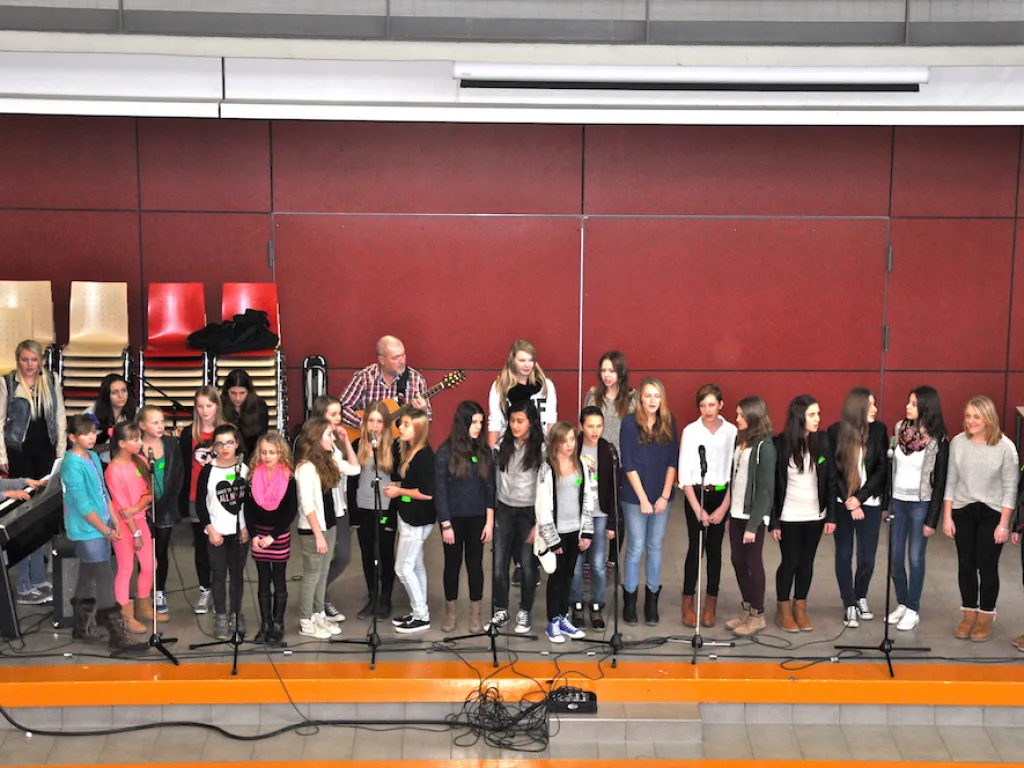 Chorgruppe singt vor der roten Wand im Foyer.